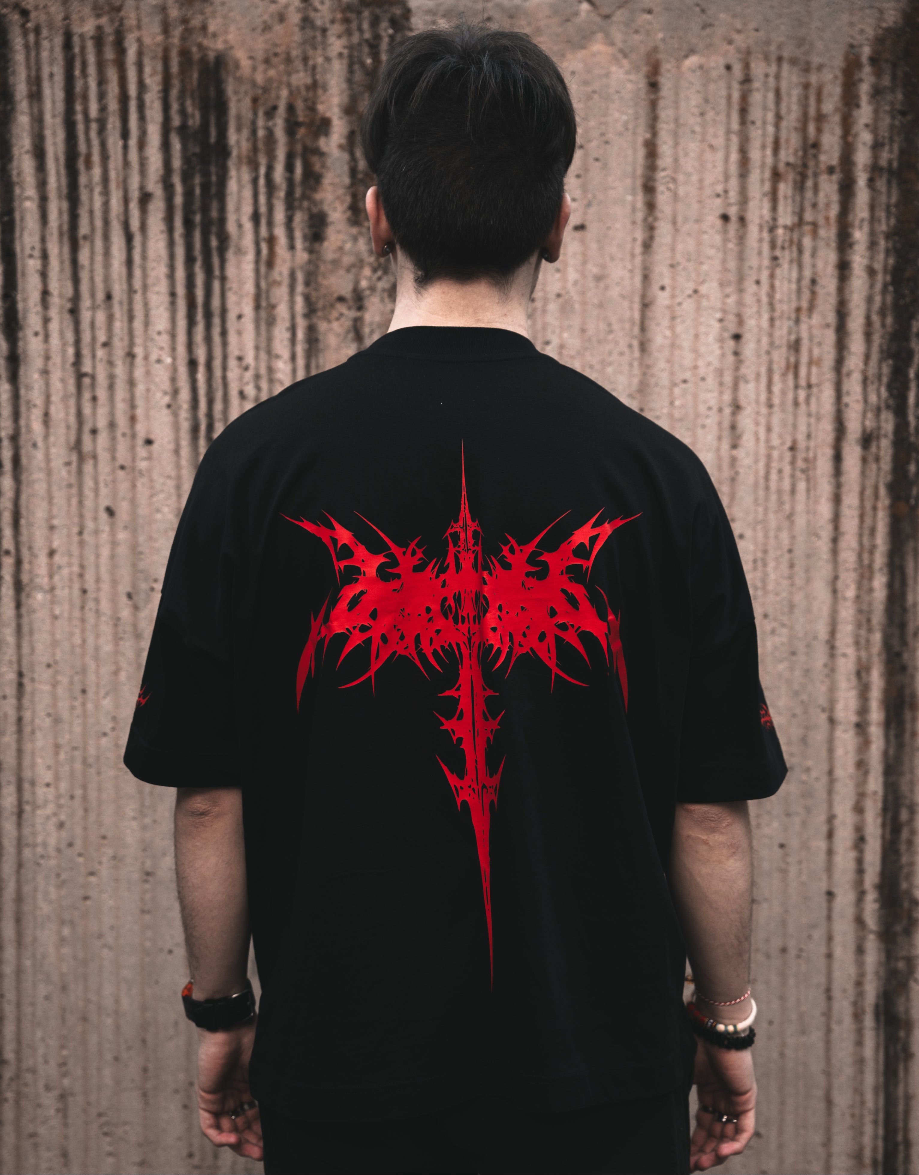 Rear view of a model wearing the ALTRUIST black oversized t-shirt featuring a red neo-tribal cyber-sigilism graphic on the chest and sleeves, styled with black cargo pants.