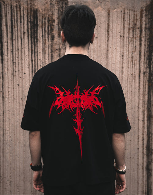 Rear view of a model wearing the ALTRUIST black oversized t-shirt featuring a red neo-tribal cyber-sigilism graphic on the chest and sleeves, styled with black cargo pants.