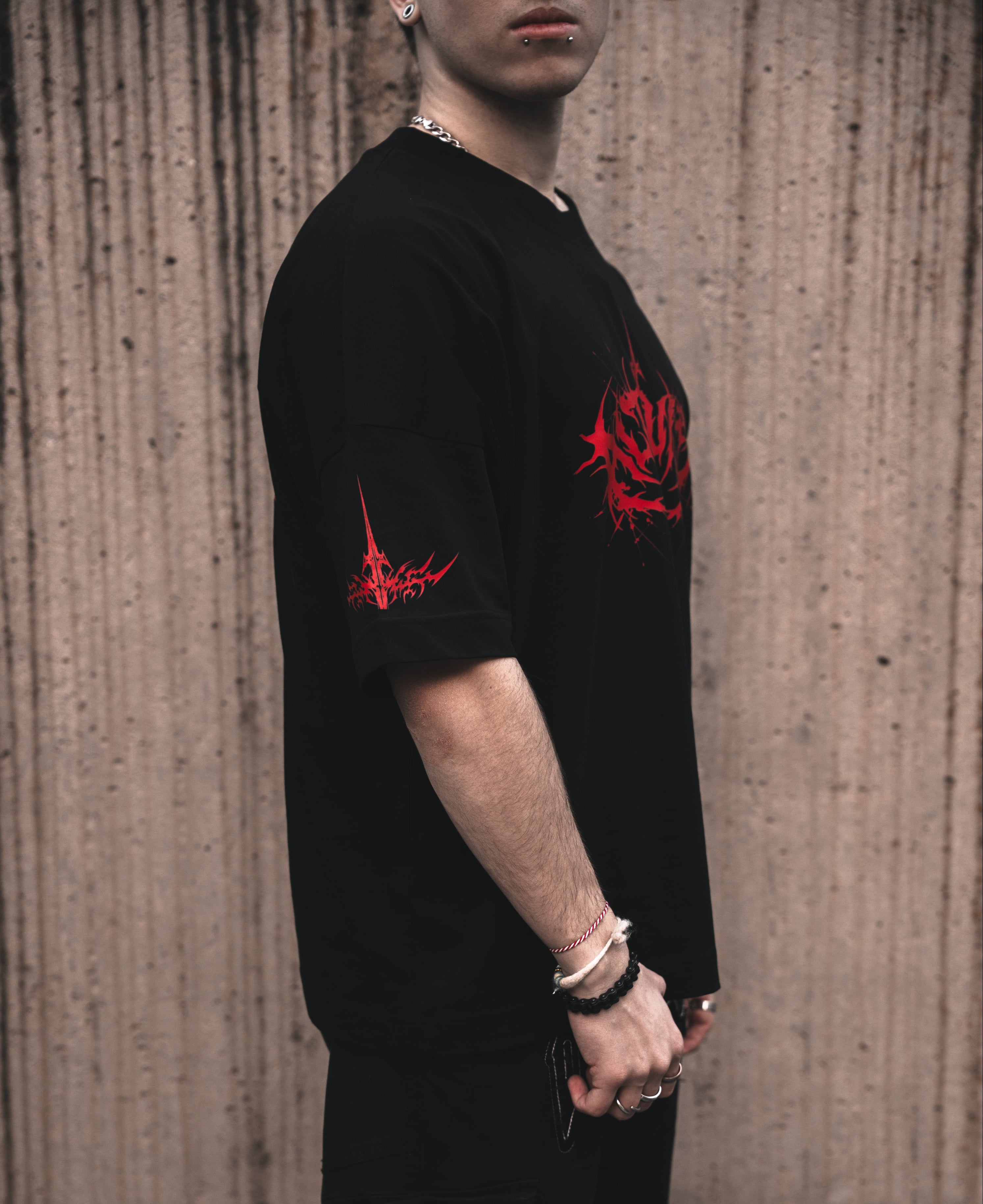 Side view of a model wearing the ALTRUIST black oversized t-shirt featuring a red neo-tribal cyber-sigilism graphic on the chest and sleeves, styled with black cargo pants.